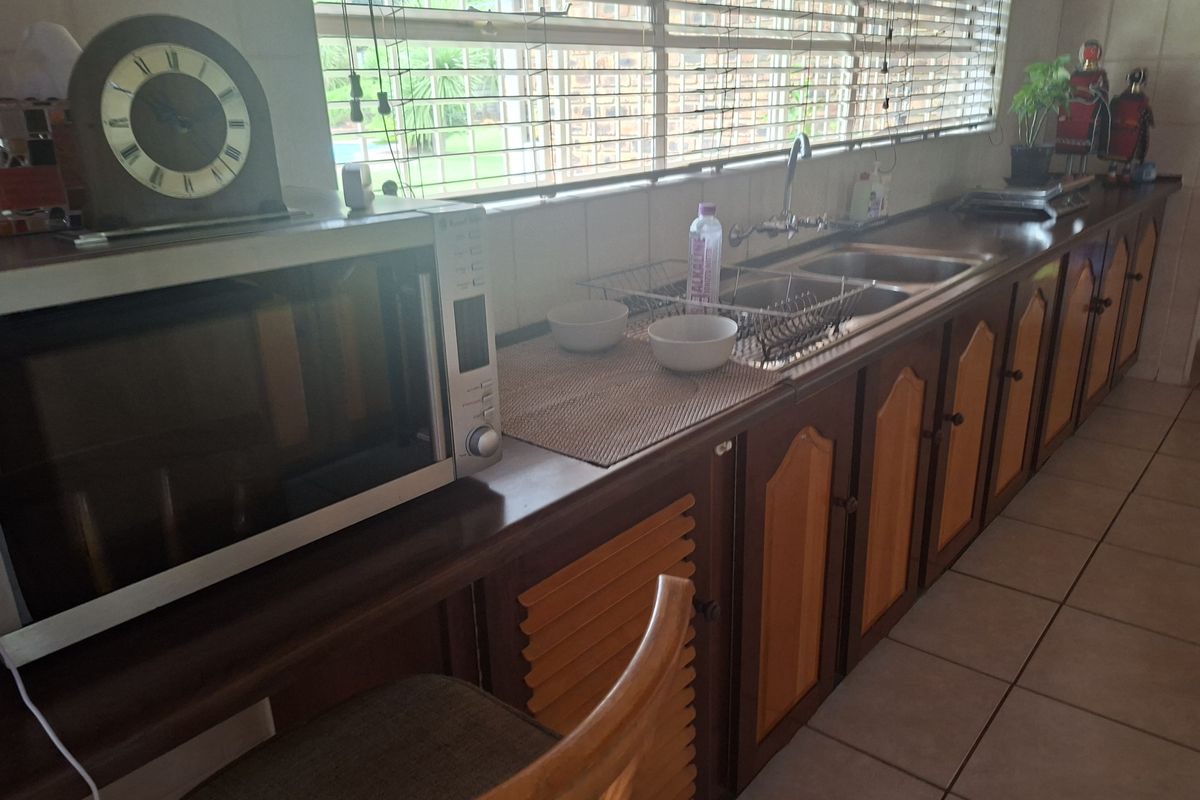 A functional kitchen featuring a long countertop, double basin sink, and traditional louvered wooden cabinetry with tiled flooring and backsplash.