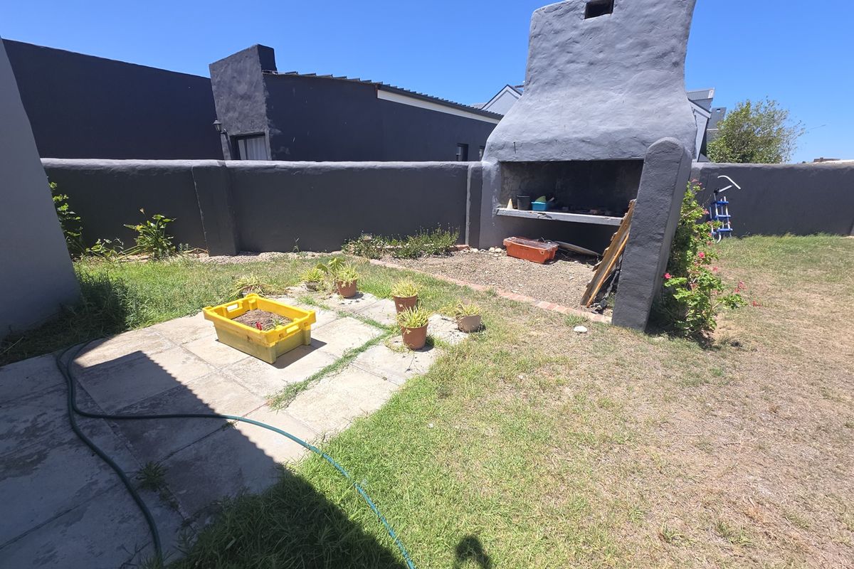 Rear garden area featuring a built-in braai, boundary wall, and paved patio space, offering potential for outdoor entertainment area development.