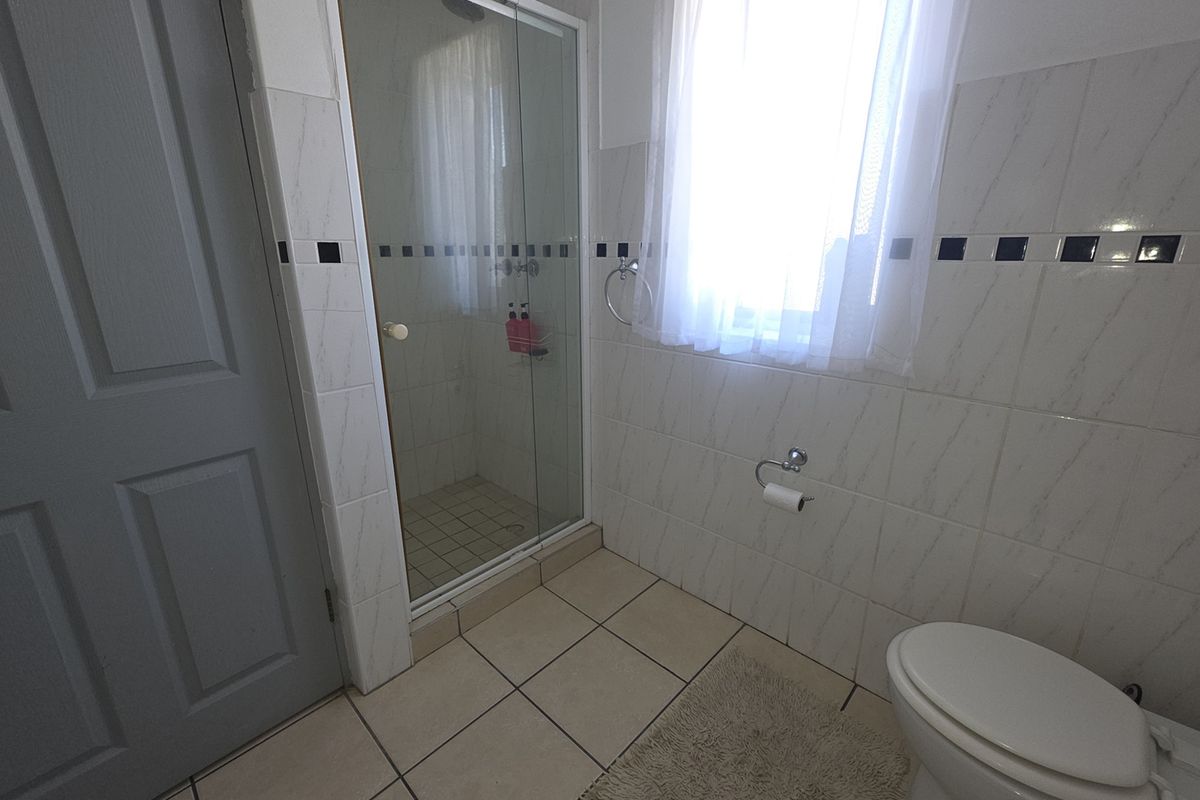 A functional bathroom featuring a glass-enclosed shower, tiled walls with decorative accents, and standard sanitary fixtures.