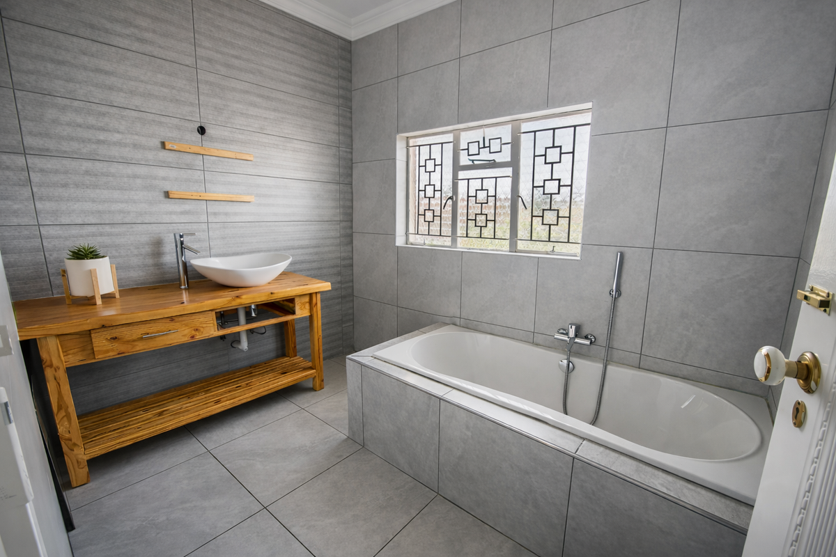 Modern bathroom featuring grey tiled walls and flooring, a built-in bathtub with handheld shower, and a wooden vanity with a vessel sink.