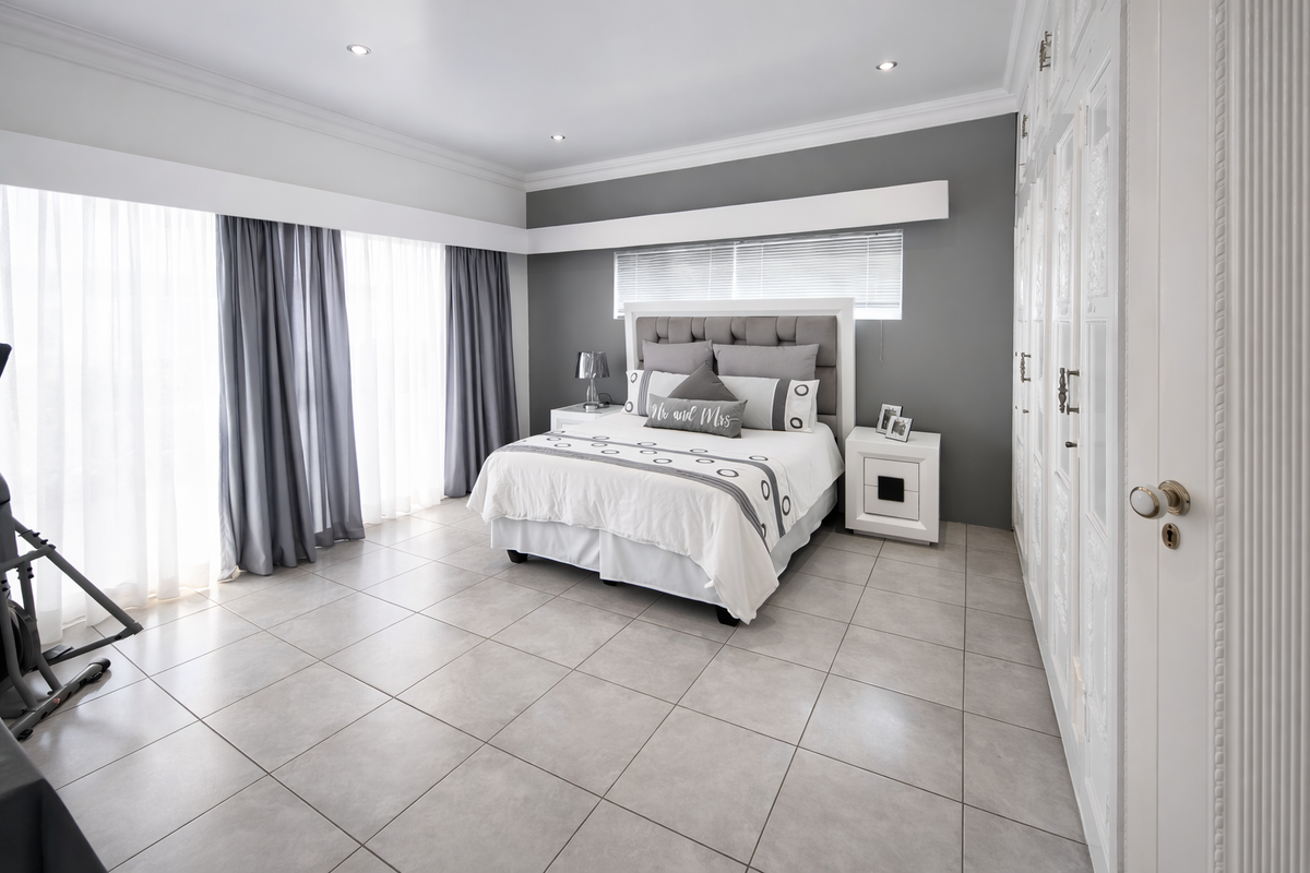 Spacious bedroom featuring neutral tiled flooring, extensive built-in cabinetry, recessed downlighting, and large windows with elegant drapery.