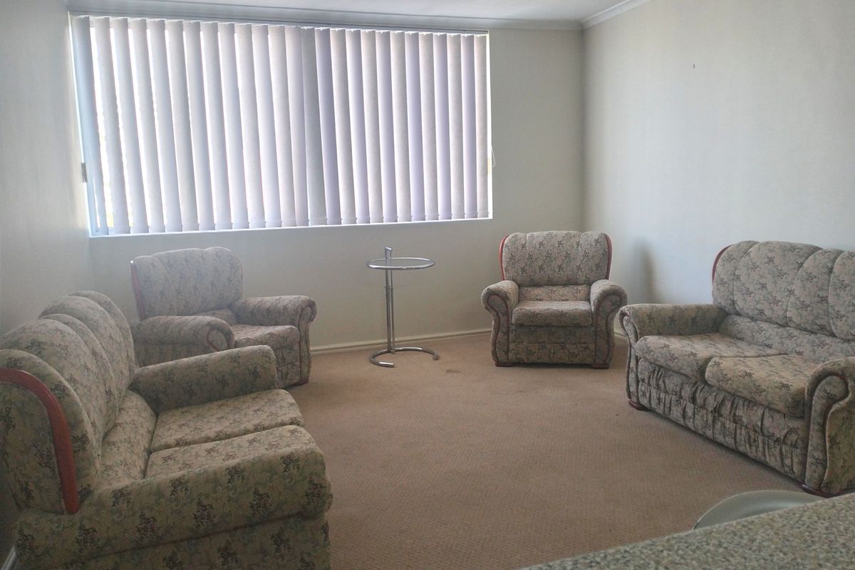 A living room area featuring neutral walls, carpet flooring, and vertical blinds, offering a blank canvas for potential interior updates.