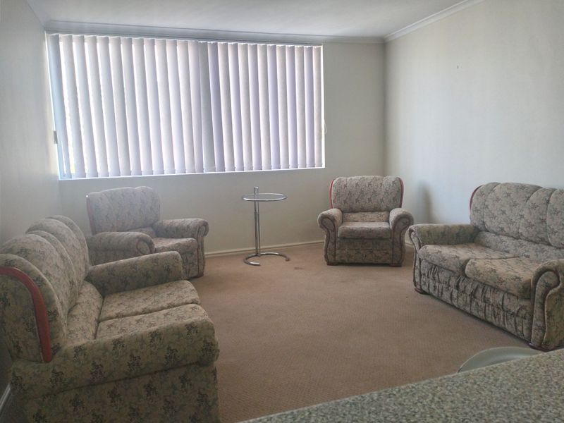 A living room area featuring neutral walls, carpet flooring, and vertical blinds, offering a blank canvas for potential interior updates.
