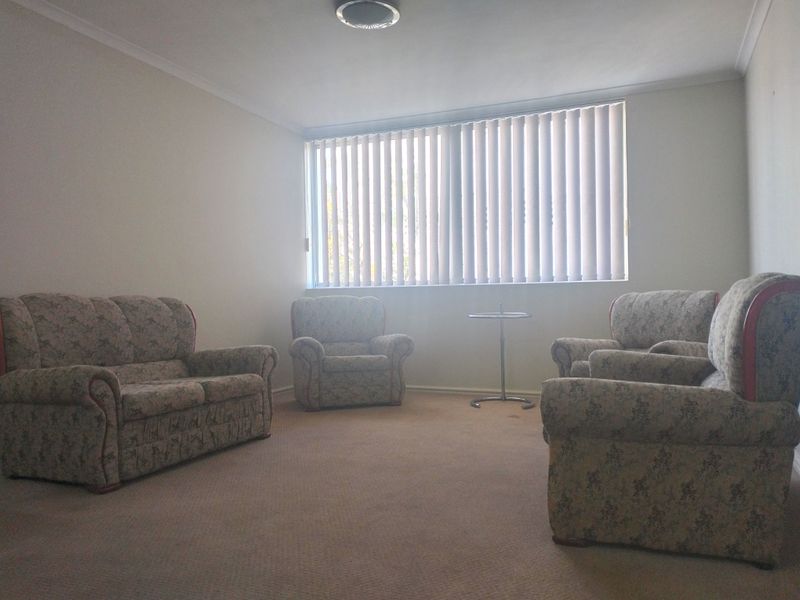 A spacious living room featuring neutral carpeting, vertical window blinds, and classic ceiling cornicing, offering a blank canvas for modern interior updates.