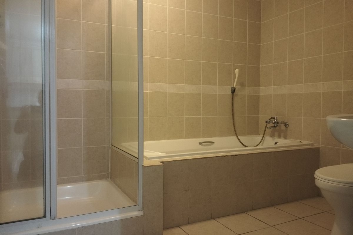 A functional bathroom featuring a separate shower enclosure, a built-in bathtub with a handheld shower mixer, and neutral ceramic tiling throughout.