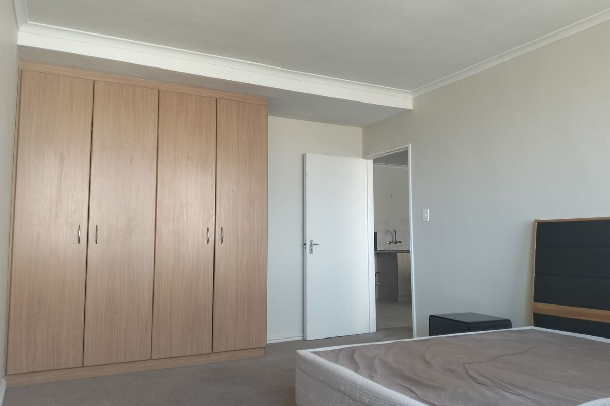 A well-maintained bedroom featuring neutral walls, carpeted flooring, and a large built-in wooden wardrobe with ample storage space.