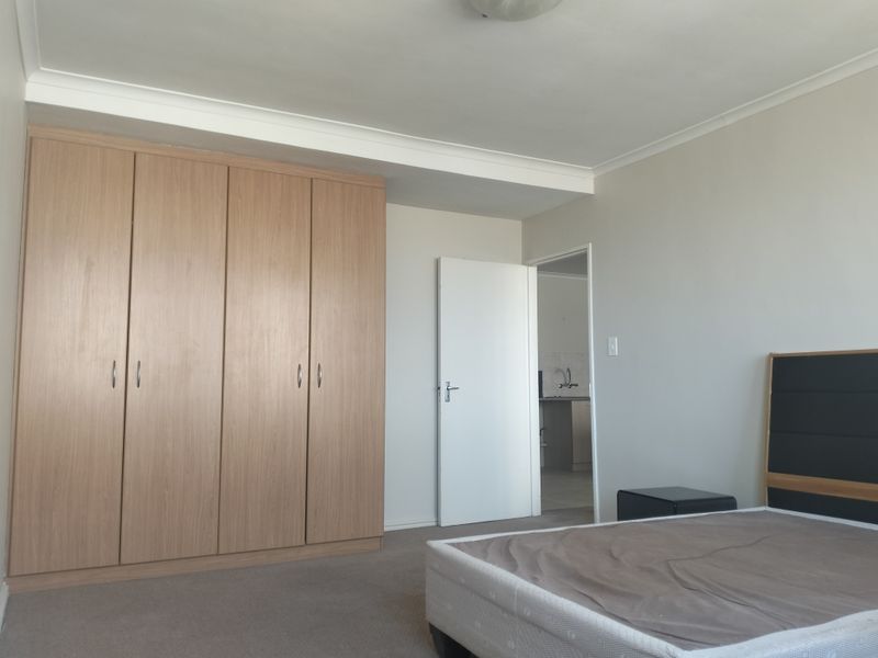 A well-maintained bedroom featuring neutral walls, carpeted flooring, and a large built-in wooden wardrobe with ample storage space.