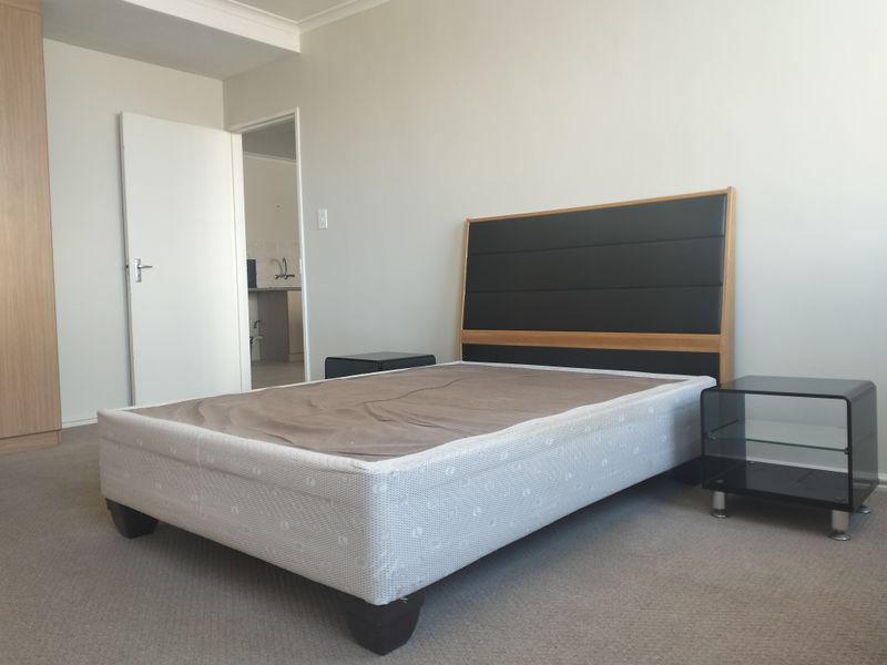 A bedroom featuring neutral walls, carpeted flooring, and a built-in wardrobe, with an adjacent view into a secondary room.
