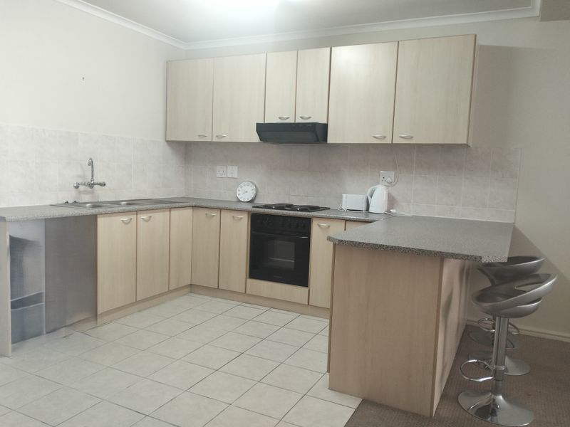 A functional kitchen featuring light wood-finish cabinetry, laminate countertops, a built-in oven with hob, and a breakfast bar area with tiled flooring.