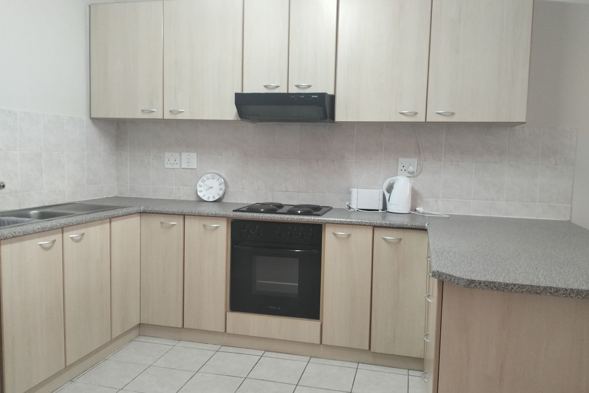 Functional kitchen featuring light wood-look cabinetry, laminate countertops, built-in oven, electric hob, extractor fan, and tiled splashback.