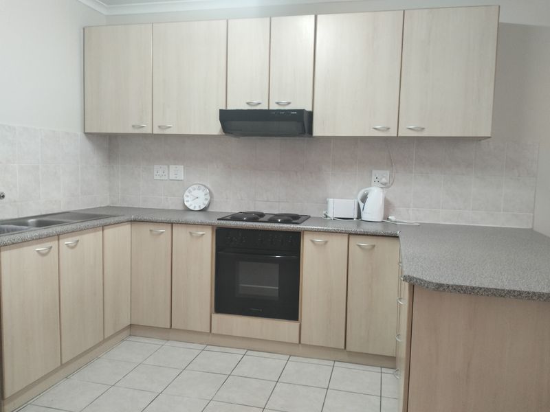 Functional kitchen featuring light wood-look cabinetry, laminate countertops, built-in oven, electric hob, extractor fan, and tiled splashback.