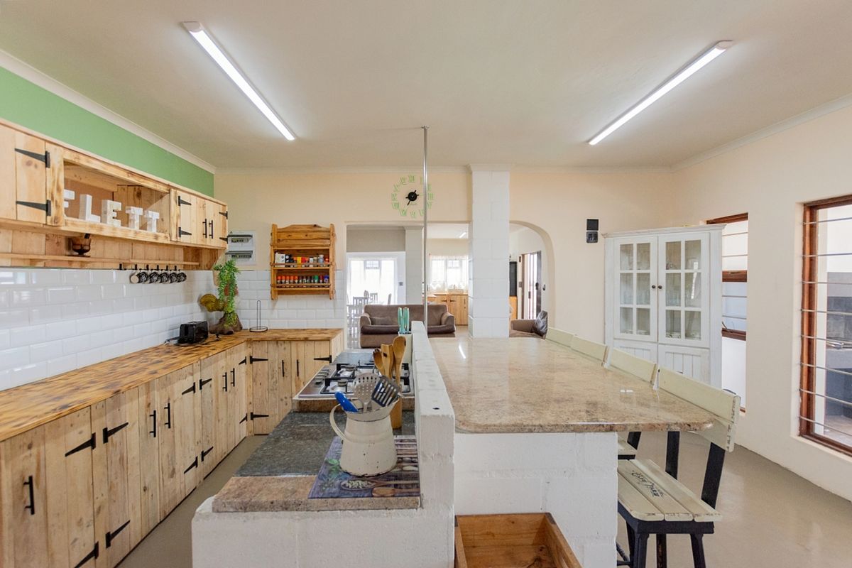 Spacious kitchen featuring rustic wooden cabinetry, subway tile backsplash, granite countertops, and a central breakfast bar island, flowing into the adjacent living area.