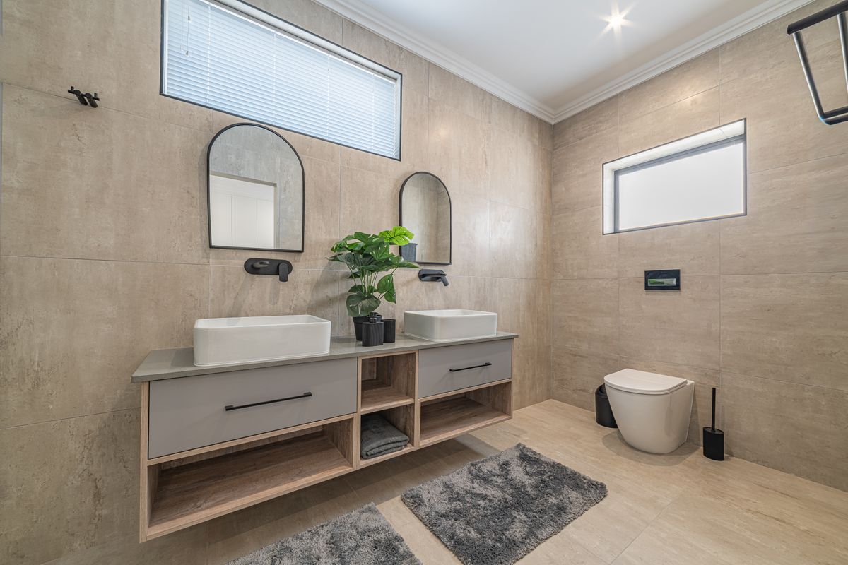 Modern bathroom featuring a double vanity with vessel sinks, wall-mounted faucets, wall-hung toilet, and neutral floor-to-ceiling tiling.