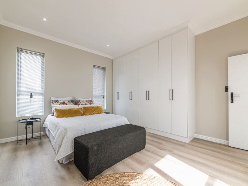 A bright and modern bedroom featuring extensive built-in cupboards, light laminate flooring, and clean neutral finishes.