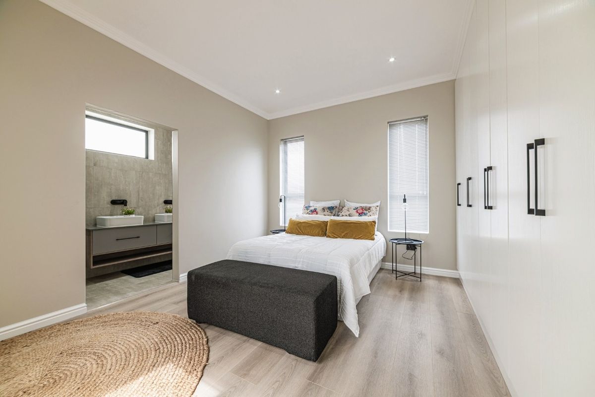 Modern bedroom featuring light laminate flooring, extensive built-in cupboards, recessed lighting, and direct access to a contemporary en-suite bathroom.