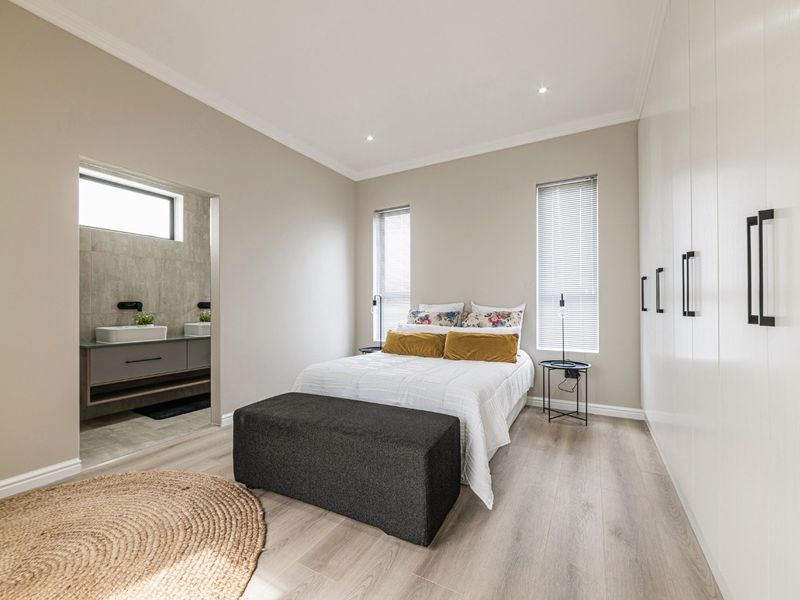 Modern bedroom featuring light laminate flooring, extensive built-in cupboards, recessed lighting, and direct access to a contemporary en-suite bathroom.