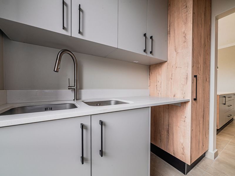 A modern, well-appointed scullery featuring sleek grey and wood-look cabinetry, a double stainless steel sink, and durable quartz countertops.