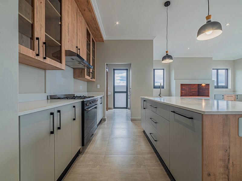 Modern kitchen featuring a large central island, stone countertops, built-in oven with gas hob, and sleek cabinetry, complemented by a built-in fireplace.