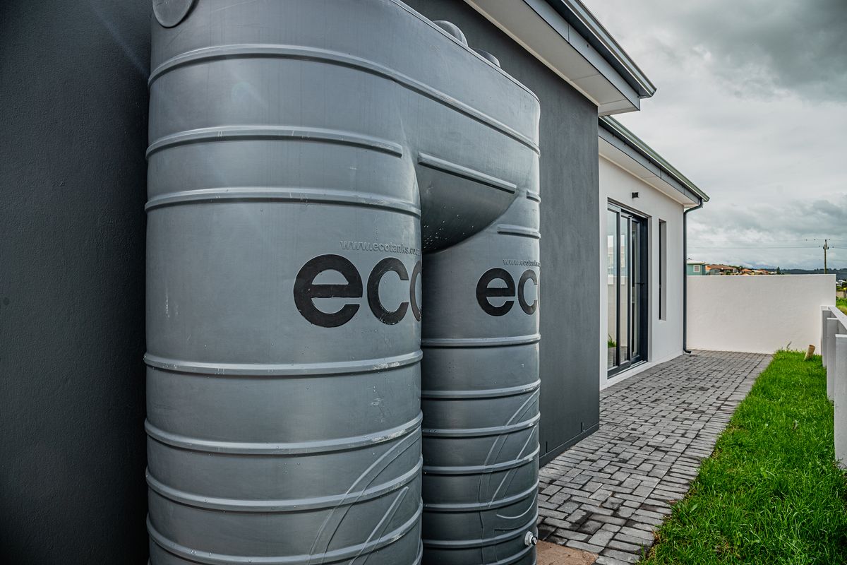 A side view of the property featuring a large grey water storage tank, paved walkway, and modern sliding glass door access.