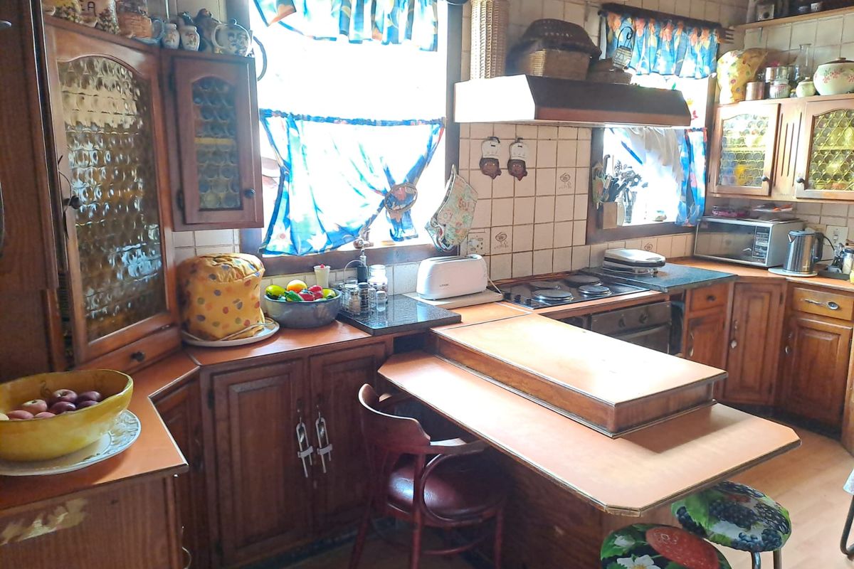 A dated kitchen featuring traditional wooden cabinetry, tiled splashbacks, a built-in hob, and an integrated extractor fan with a breakfast nook area.