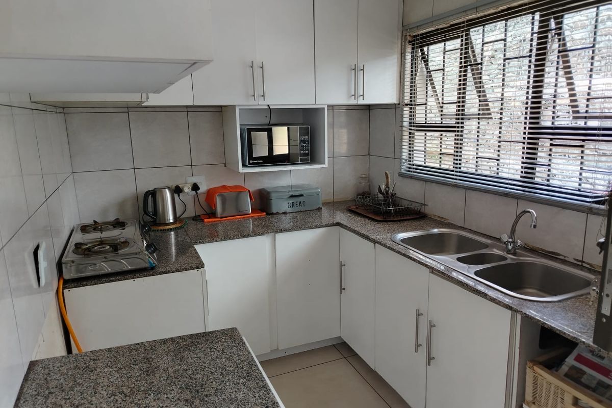 A functional kitchen featuring granite countertops, white cabinetry, a double stainless steel sink, and a tiled backsplash with built-in microwave storage.