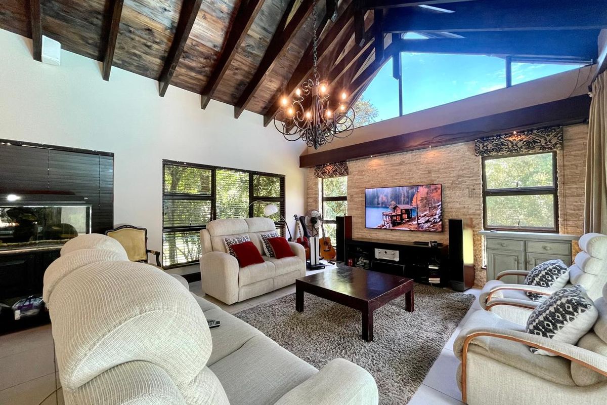 Spacious living room featuring a high vaulted timber-beamed ceiling, exposed brick feature wall, and large windows providing ample natural light.