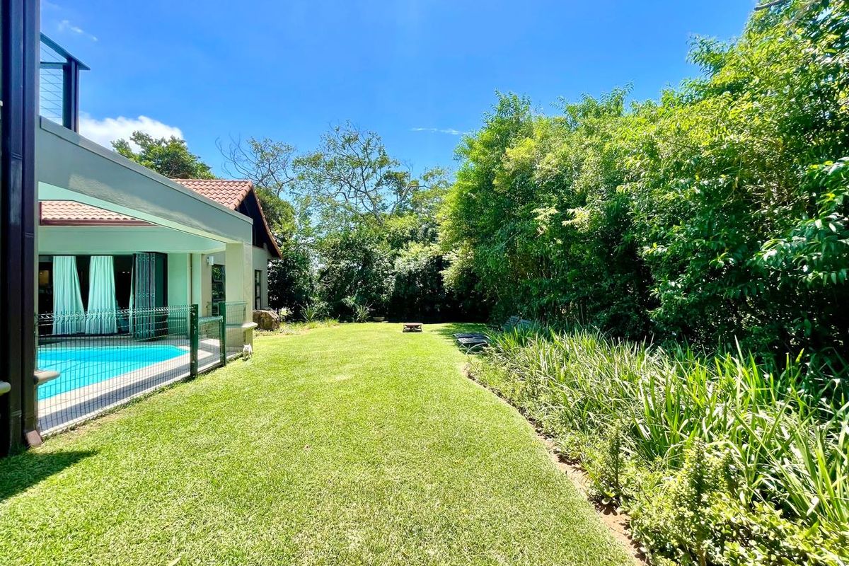 A spacious rear garden featuring a well-maintained lawn, mature perimeter landscaping, and a fenced swimming pool area adjacent to the home.