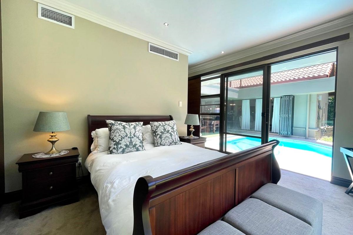 Spacious bedroom featuring ducted air conditioning, neutral finishes, and large sliding glass doors providing direct access to the outdoor pool area.
