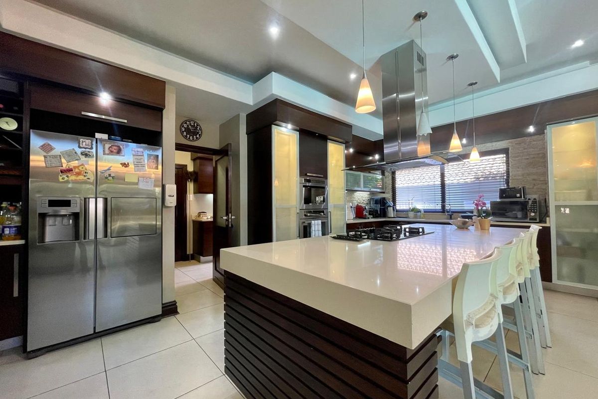 Modern kitchen featuring a large central island with stone countertop, built-in oven, stainless steel extractor fan, and dark wood cabinetry.