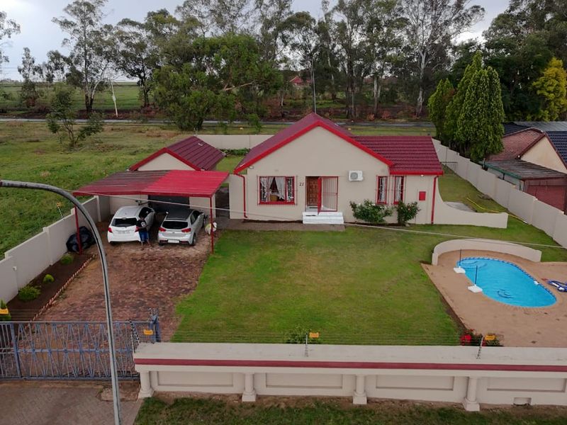 Aerial view of a residential property featuring a swimming pool, paved driveway, carport, and secure perimeter wall with electric fencing.