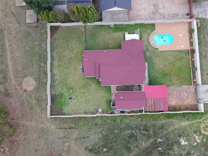 Aerial view of a residential property featuring a tiled roof house, a swimming pool, and a spacious garden enclosed by a perimeter wall.