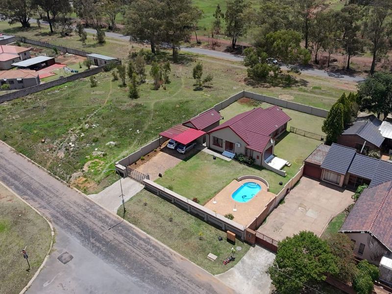 Aerial view of a residential property featuring a swimming pool, carport, and enclosed garden area within a suburban setting.
