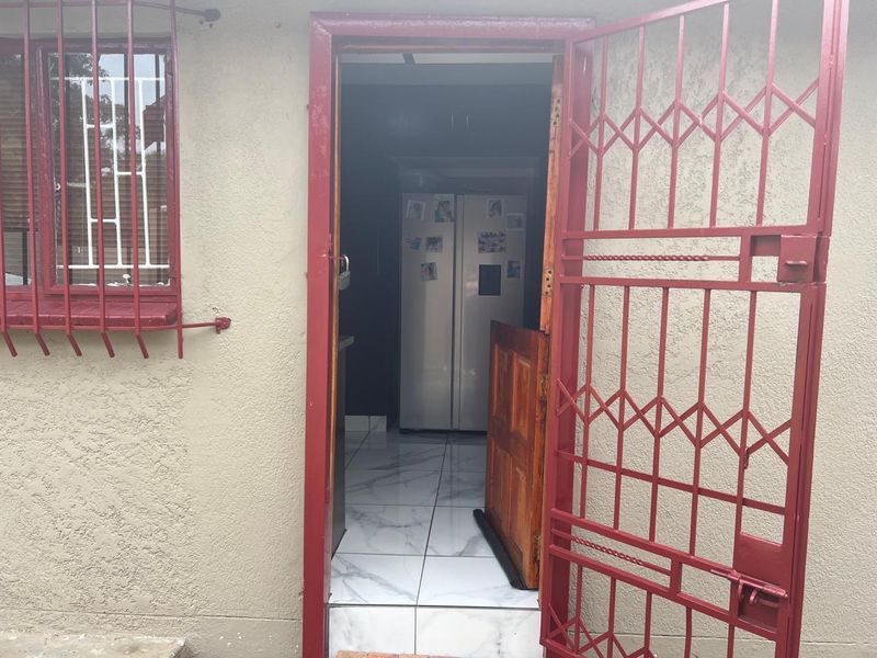 Exterior view of a home entrance featuring a red security gate, security bars on the window, and tiled flooring visible through the doorway.
