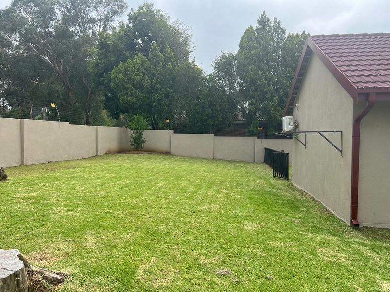 A spacious rear garden featuring a well-maintained lawn, perimeter wall with electric fencing, and a side elevation of the house with an external air conditioning unit.