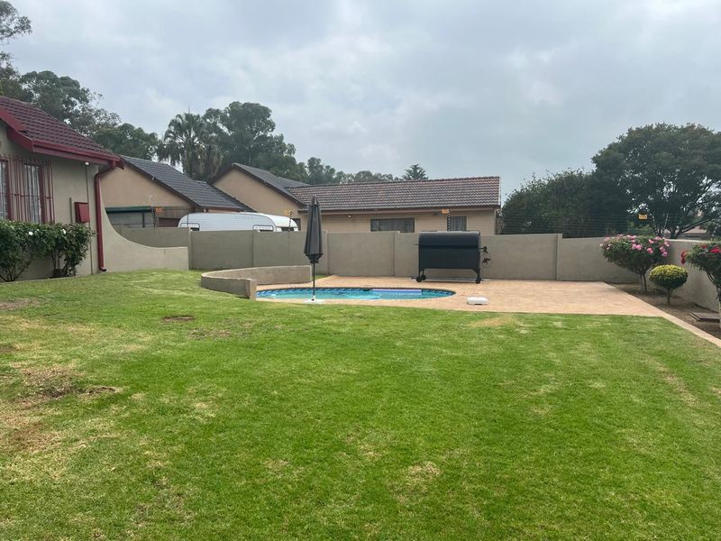 A private backyard featuring a swimming pool, paved patio area, and secure perimeter walling with electric fencing.