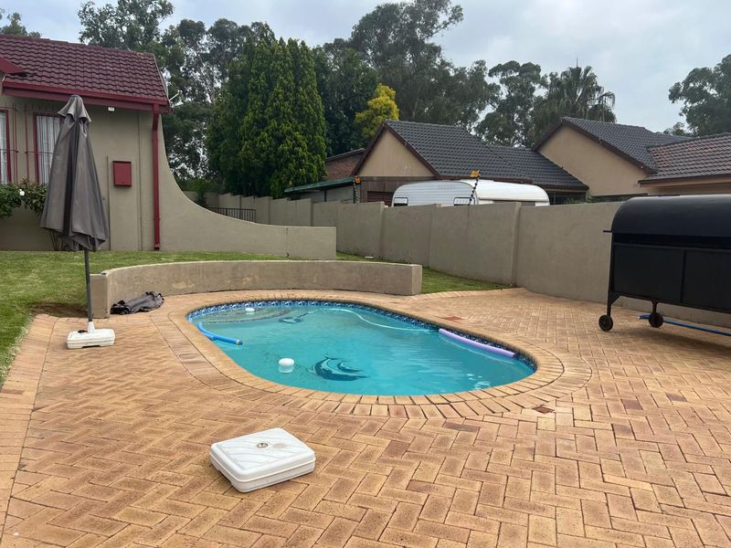Outdoor pool area featuring a swimming pool with brick paved surround and a curved retaining wall, enclosed by a perimeter boundary wall.