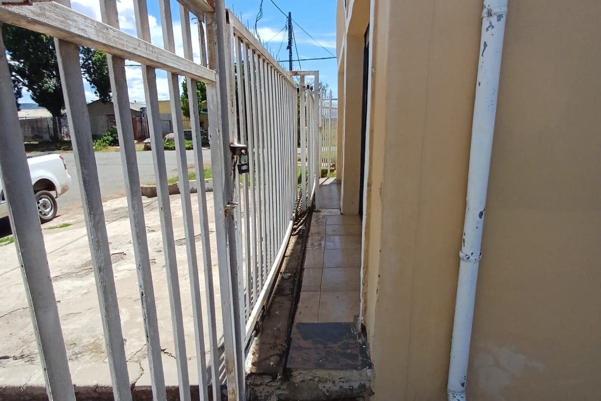 Side exterior walkway featuring a metal security gate, tiled flooring, and a painted exterior wall with a vertical downpipe.