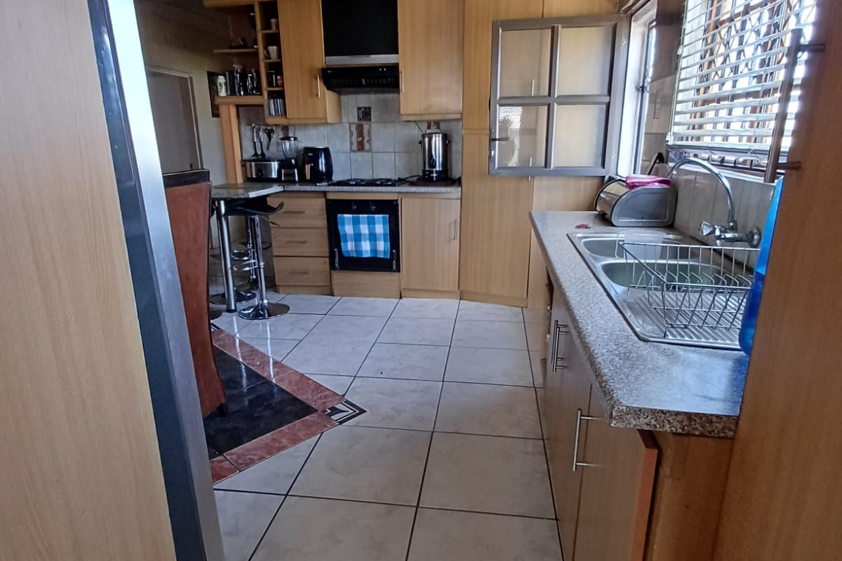 A functional kitchen featuring wooden cabinetry, built-in oven and hob, double sink, and tiled flooring with decorative ceiling detailing.