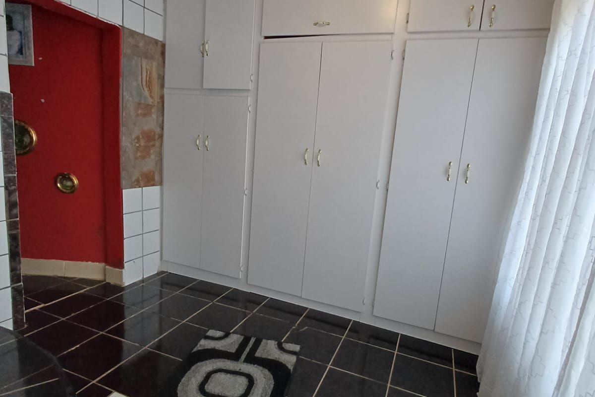 A functional room featuring extensive built-in white cabinetry, dark tiled flooring, and a distinct red-painted arched entryway.