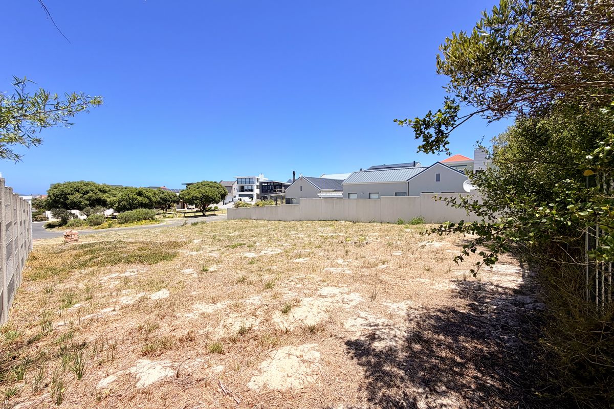 A vacant residential plot featuring sandy terrain, boundary walls, and surrounding neighborhood views, ideal for new construction.