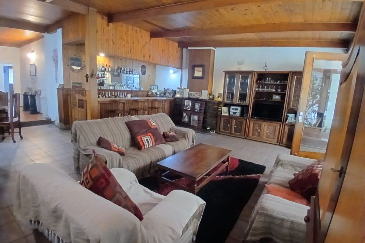 Spacious living room featuring exposed timber ceiling beams, tiled flooring, and a built-in bar area with wood paneling.