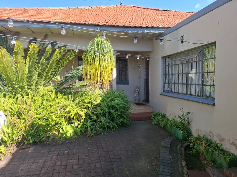 A rear courtyard area featuring paved flooring, terracotta roof tiles, and steel-framed windows with security bars, set against a rendered exterior wall.