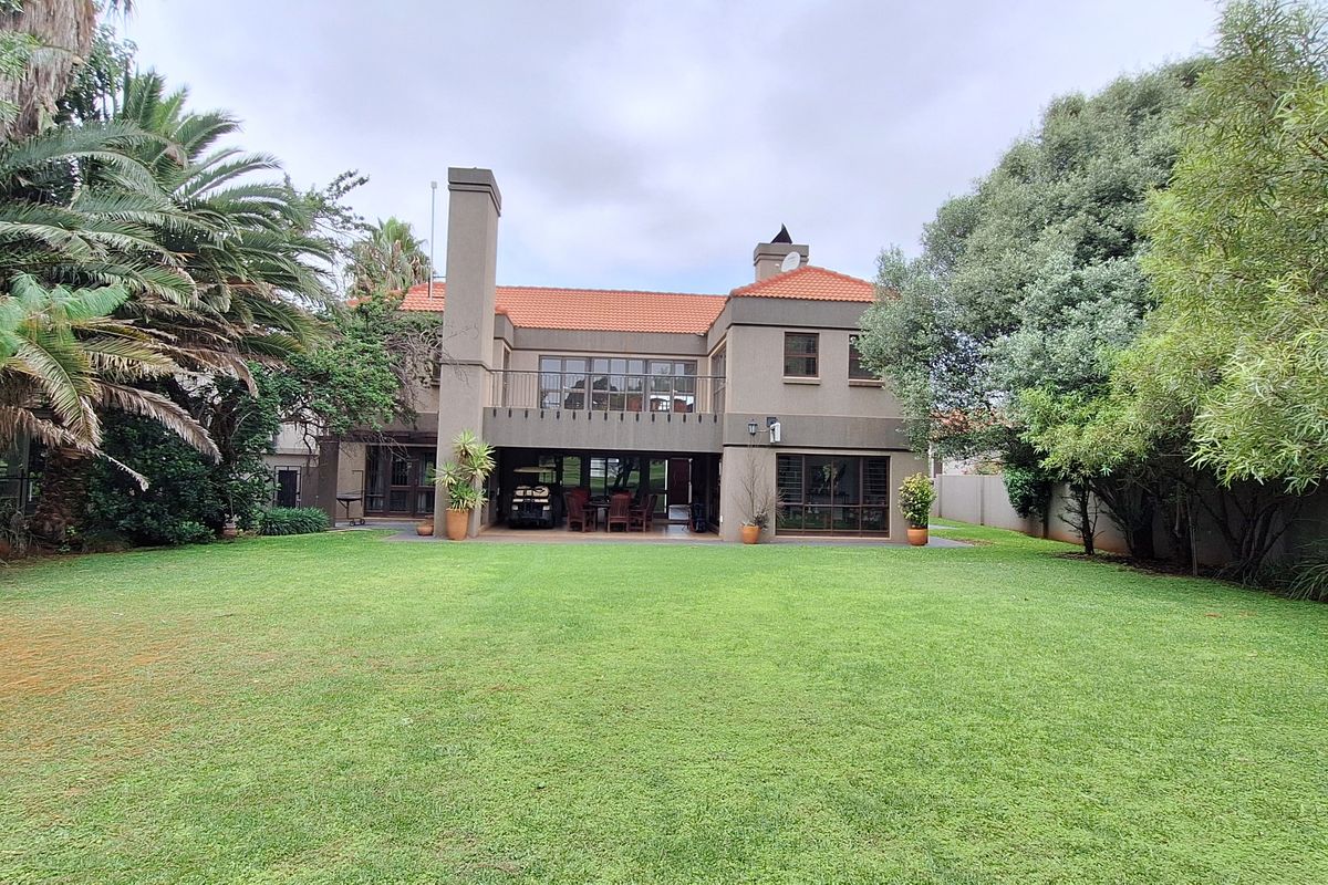 Rear view of a two-story house featuring a spacious lawn, covered patio, upper balcony, and traditional terracotta tile roof.