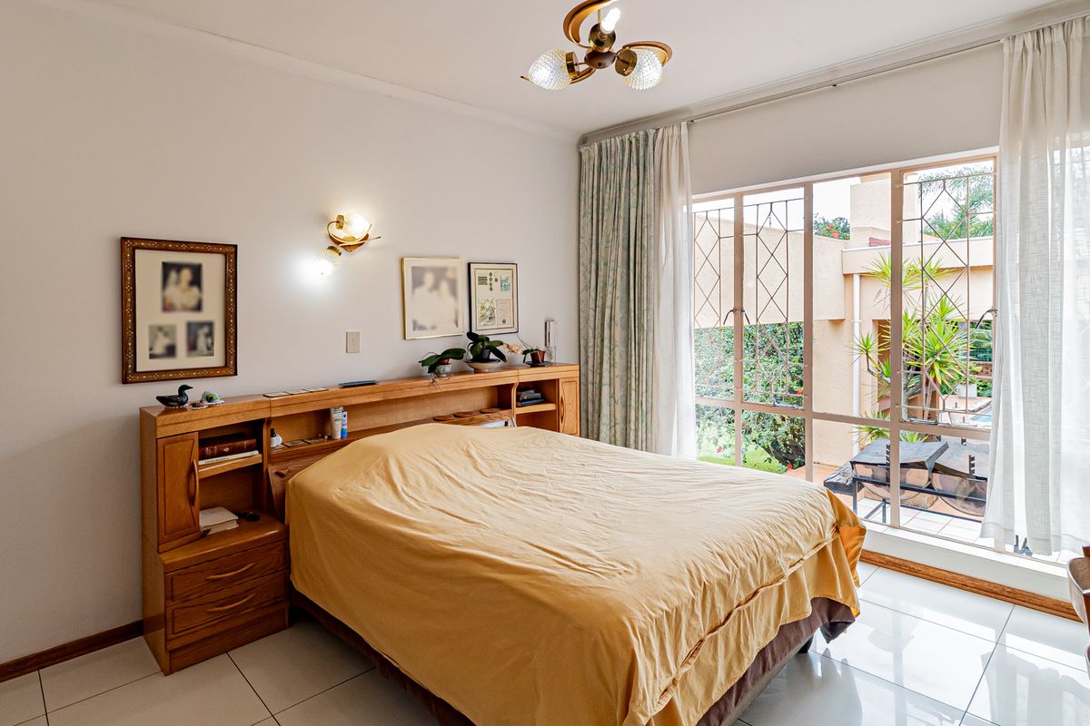 A well-lit bedroom featuring tiled floors, a built-in wooden headboard, and large glass doors providing access to the outdoor area.