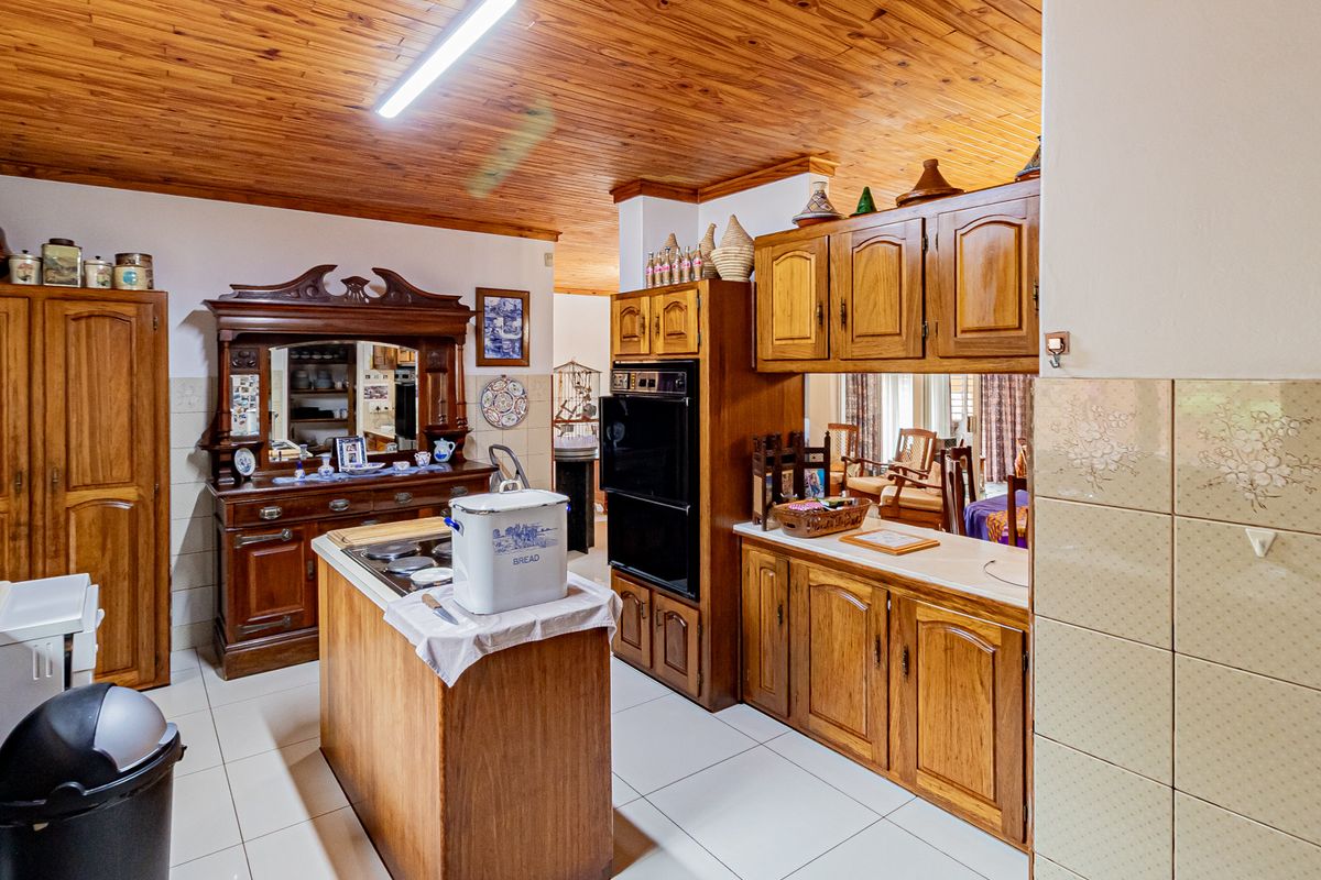 A traditional kitchen featuring extensive timber cabinetry, a central island, double wall oven, and a warm timber-clad ceiling with tiled flooring.