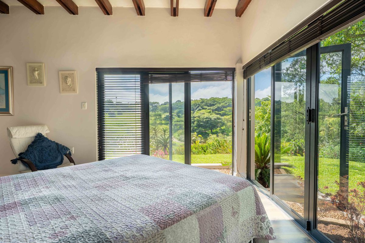 Bright bedroom featuring exposed timber ceiling beams and large aluminium sliding doors that open to a scenic garden view.