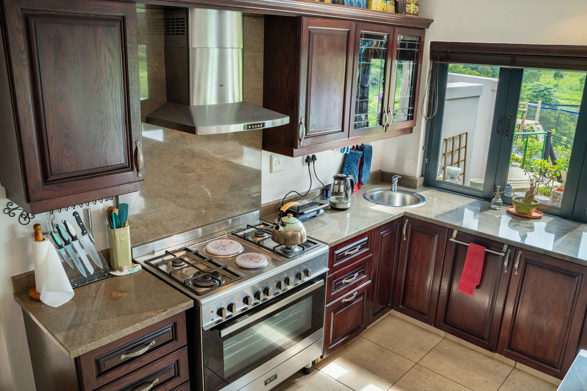A well-maintained kitchen featuring dark wood cabinetry, granite countertops, a stainless steel gas stove, and an integrated extractor fan with natural light.