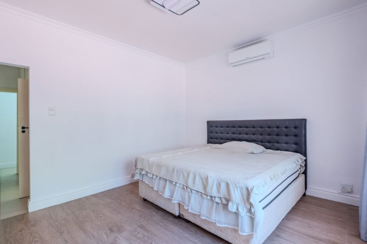 A clean and well-maintained bedroom featuring light-toned laminate flooring, crisp white walls, and a wall-mounted split-system air conditioning unit.