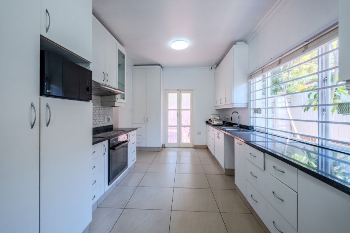 A functional galley-style kitchen featuring white cabinetry, granite countertops, built-in oven, extractor fan, and tiled flooring with direct access to the exterior.