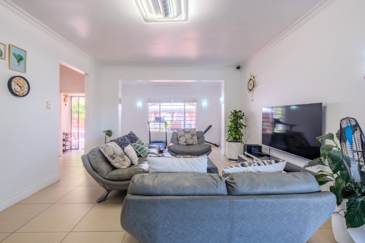 A spacious, well-lit living room featuring neutral tiled flooring, coved ceilings, and recessed lighting, providing a comfortable and functional family living space.